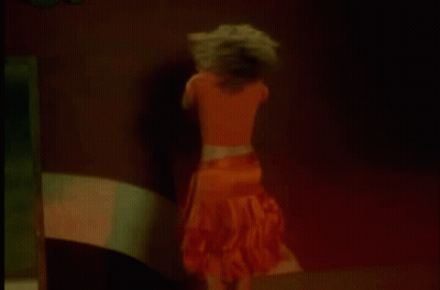 A Woman In An Orange Skirt Is Dancing In A Dark Room . GIF