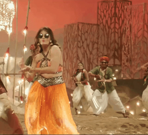 A Woman In An Orange Skirt Is Dancing With A Group Of People GIF