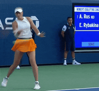A Woman In An Orange Skirt Is Playing Tennis On A Tennis Court GIF