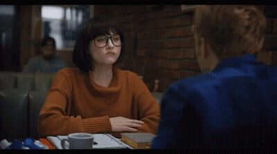 A Woman In An Orange Sweater Sits At A Table With A Man GIF