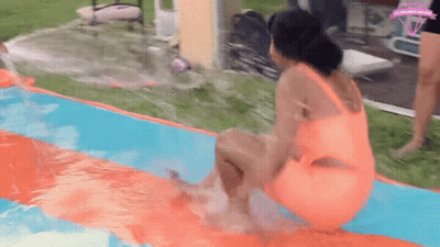 A Woman In An Orange Swimsuit Is Sitting On Top Of A Water Slide In A Pool . GIF