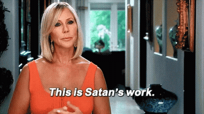 A Woman In An Orange Tank Top Is Standing In A Hallway And Saying This Is Satan 'S Work . GIF