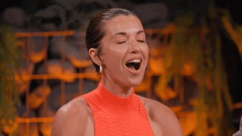 A Woman In An Orange Top With Her Mouth Wide Open GIF