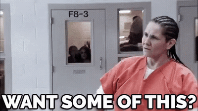 A Woman In An Orange Uniform Is Standing In Front Of A Door And Asking , `` Want Some Of This ? '' GIF