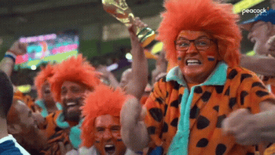 A Woman In An Orange Wig Is Holding A Trophy In A Crowd Of People At A Soccer Game . GIF
