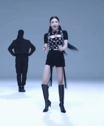 A Woman In Black Shorts And Boots Is Dancing In Front Of A Man GIF