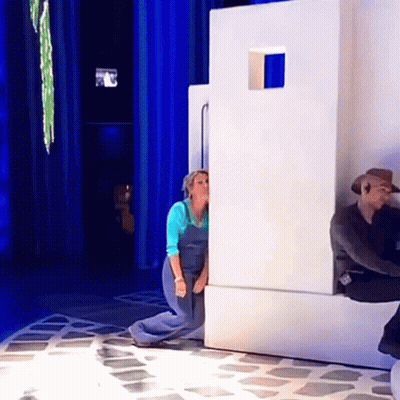A Woman In Blue Overalls Is Peeking Out From Behind A Wall GIF