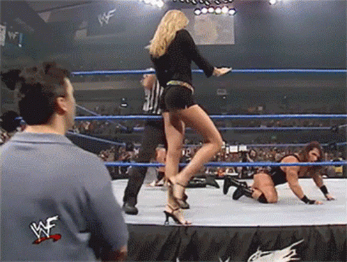 A Woman In High Heels Is Standing In A Wrestling Ring With A W Logo On The Bottom GIF
