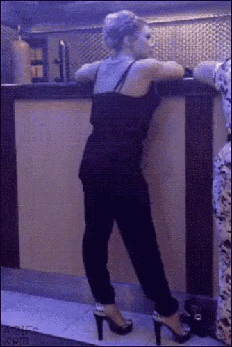 A Woman In High Heels Leans Against A Bar GIF