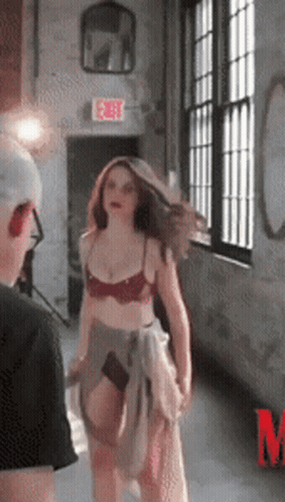 A Woman In Lingerie Is Standing In Front Of A Window With An Exit Sign Above Her GIF