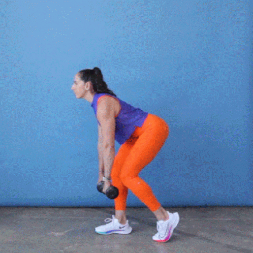 A Woman In Orange Pants And A Purple Tank Top Is Holding A Dumbbell In Her Hands . GIF