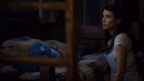 A Woman In Overalls And A White Shirt Is Standing In A Dark Room GIF
