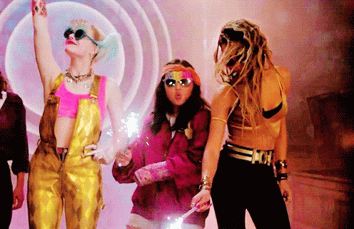A Woman In Overalls Is Holding A Sparkler In Her Hand While Standing Next To Two Other Women GIF