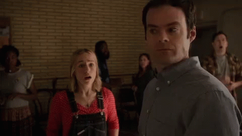 A Woman In Overalls Is Standing Next To A Man In A Room . GIF