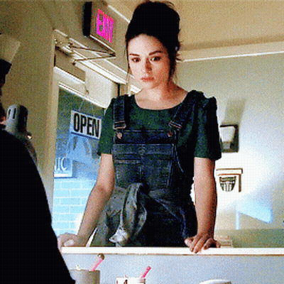 A Woman In Overalls Stands In Front Of A Sign That Says Open GIF