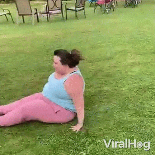 A Woman In Pink Pants Is Sitting On The Grass In A Yard . GIF