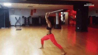 A Woman In Red Pants Is Holding A Sword In A Gym With The Words Awesome On The Bottom GIF