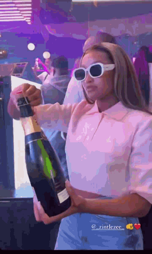 A Woman In Sunglasses Is Holding A Bottle Of Champagne . GIF