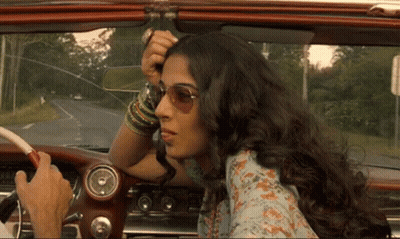 A Woman In Sunglasses Is Sitting In A Car With A Man Driving GIF