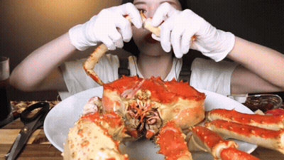 A Woman In White Gloves Is Eating A Large Red Crab GIF