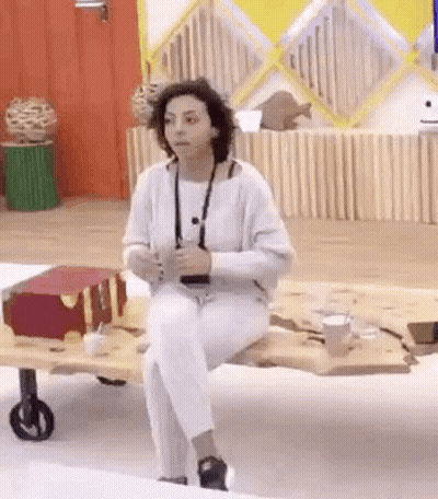 A Woman In White Pants Is Sitting On A Wooden Table . GIF