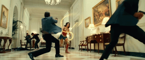 A Woman In Wonder Woman 'S Costume Is Surrounded By Men In Suits GIF