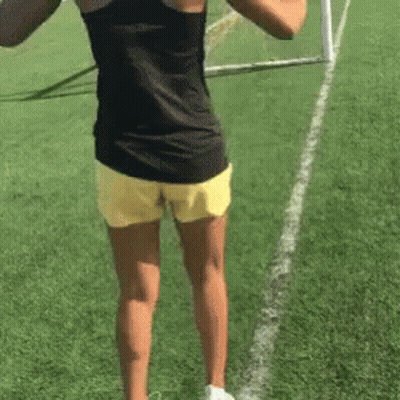 A Woman In Yellow Shorts And A Black Tank Top Is Standing On A Field . GIF