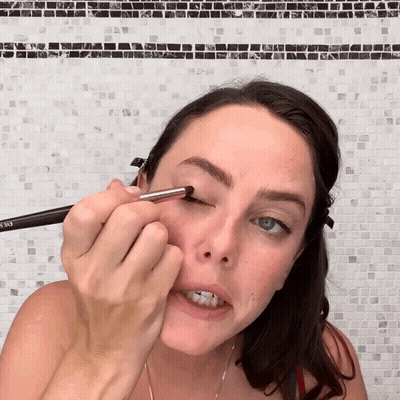 A Woman Is Applying Eyeliner With A Brush That Says Eyeliner GIF