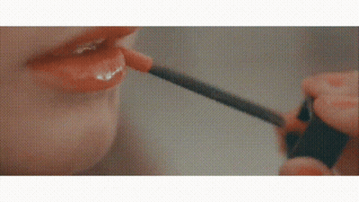 A Woman Is Applying Lip Gloss With A Brush To Her Lips . GIF