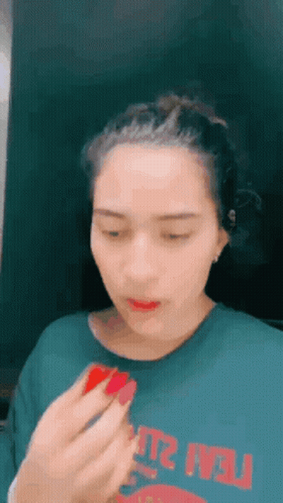 A Woman Is Applying Lipstick To Her Lips While Wearing A Green T-Shirt . GIF