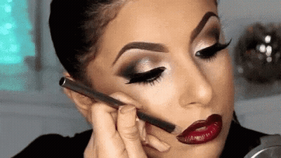 A Woman Is Applying Makeup To Her Face . GIF