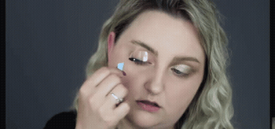A Woman Is Applying Mascara To Her Eyelashes With A Brush . GIF