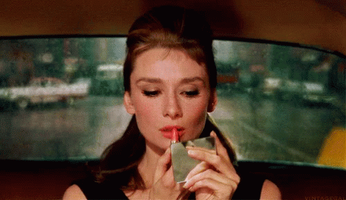 A Woman Is Applying Red Lipstick While Holding A Lighter . GIF