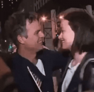 A Woman Is Being Hugged By A Man In A Crowd . GIF