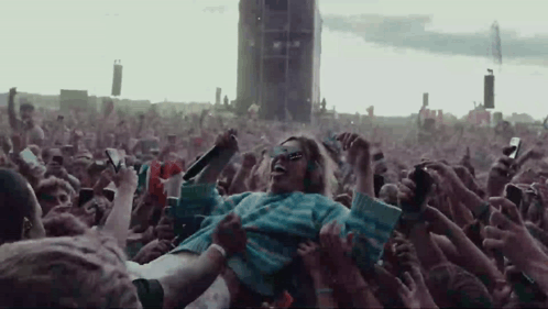 A Woman Is Being Lifted In The Air By A Crowd Of People At A Music Festival . GIF