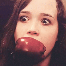 A Woman Is Biting Into A Red Apple With Her Eyes Wide Open GIF