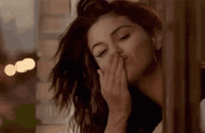 A Woman Is Blowing A Kiss While Standing Next To A Window . GIF