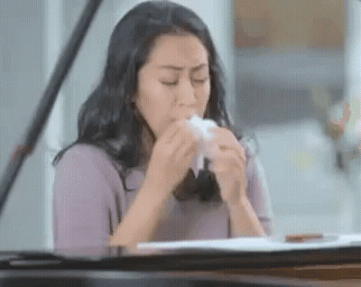 A Woman Is Blowing Her Nose With A Tissue While Sitting At A Piano . GIF