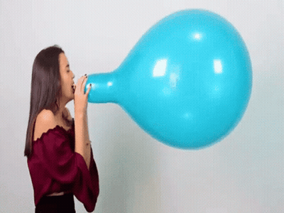 A Woman Is Blowing Up A Large Blue Balloon With Her Mouth . GIF