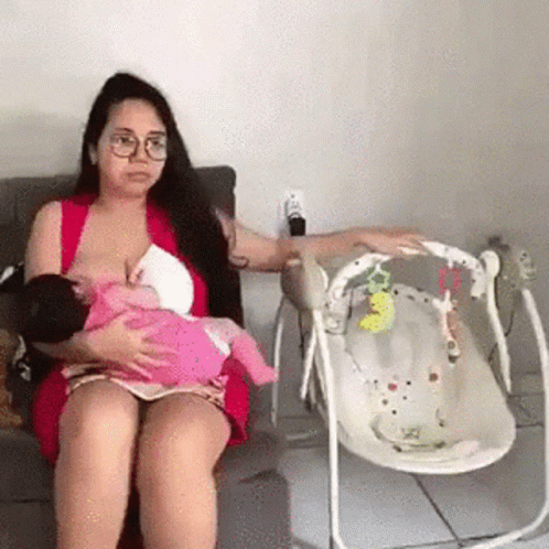 A Woman Is Breastfeeding A Baby While Sitting In A Chair . GIF