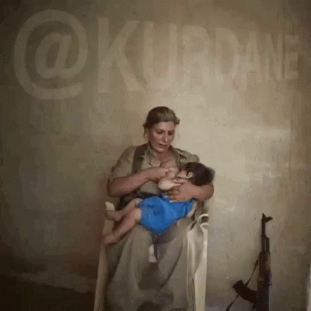 A Woman Is Breastfeeding A Baby While Sitting In Front Of A Wall That Says @Kurdane GIF