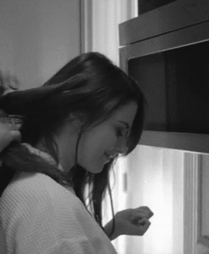 A Woman Is Brushing Her Hair In A Black And White Photo While Standing In Front Of A Microwave . GIF