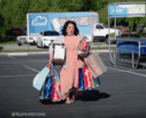 A Woman Is Carrying Shopping Bags In A Parking Lot GIF