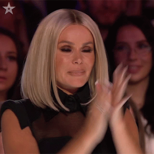 A Woman Is Clapping Her Hands In A Crowd Of People . GIF