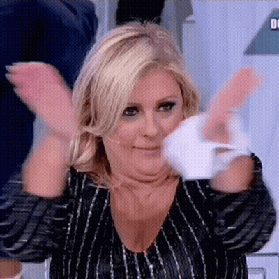 A Woman Is Clapping Her Hands In The Air While Wearing A Black And Silver Striped Shirt . GIF