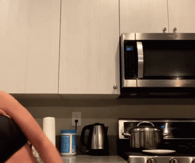 A Woman Is Cooking In A Kitchen With A Pot On The Stove And A Microwave That Has The Time Set At 10:22 GIF