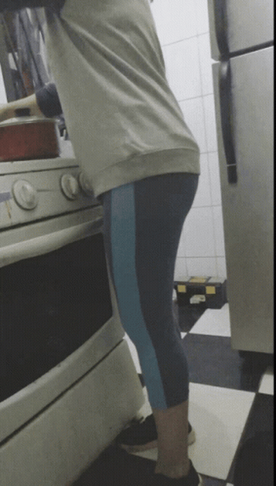 A Woman Is Cooking On A Stove In A Kitchen With A Refrigerator In The Background GIF