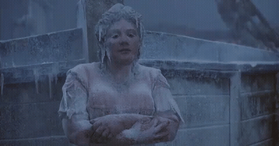 A Woman Is Covered In Ice And Is Standing With Her Arms Crossed In Front Of A Fence . GIF