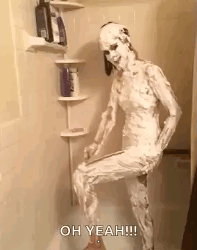 A Woman Is Covered In Shaving Cream And Standing In A Shower . GIF
