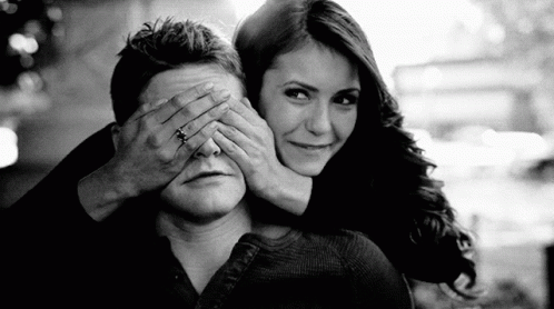 A Woman Is Covering A Man 'S Eyes With Her Hands . GIF